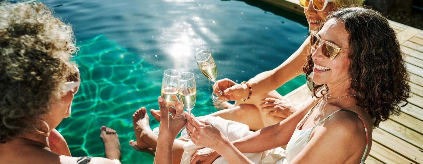 a group of women sitting by a pool with drinks